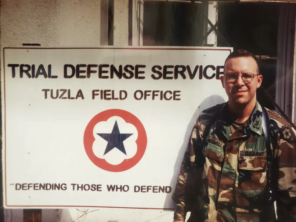 A military personnel stands beside a sign for the Tuzla Field Office.
